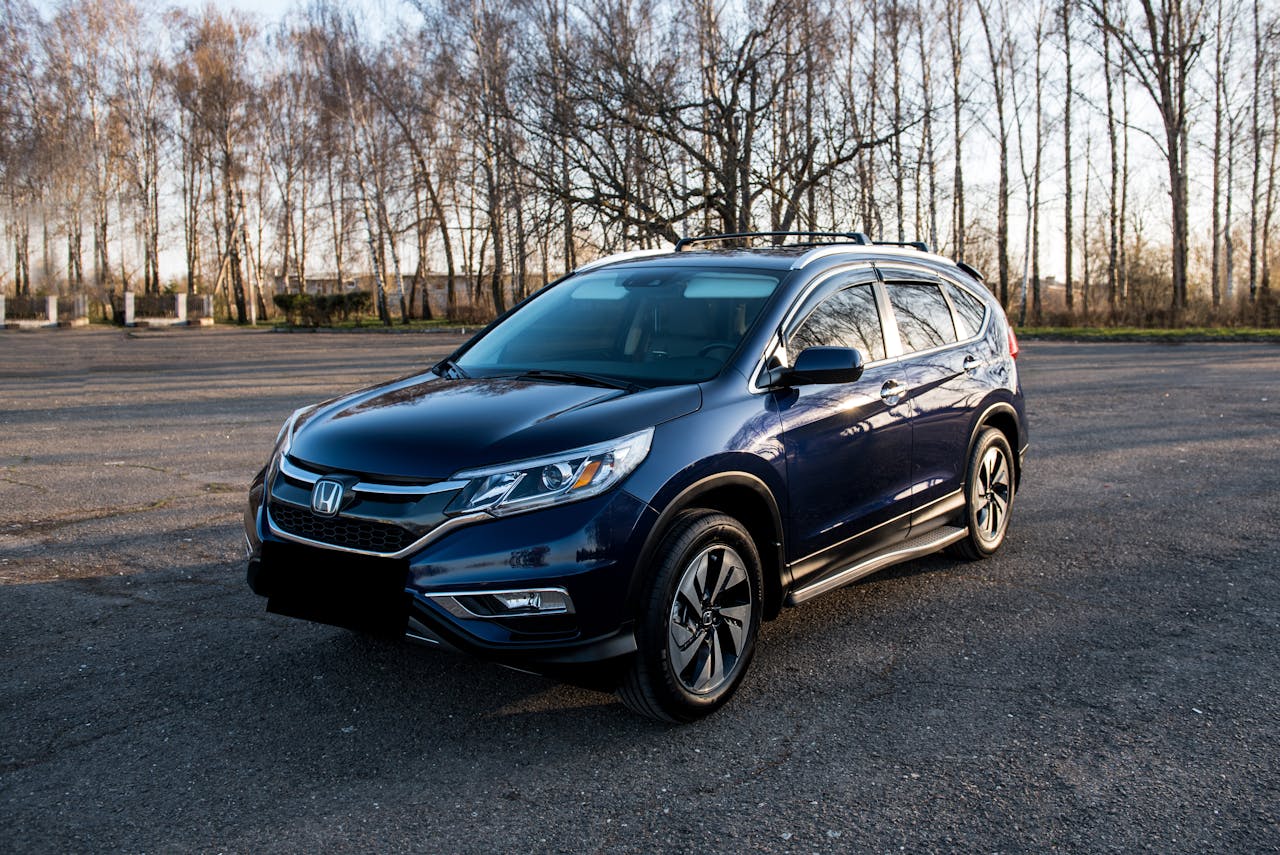 Home A sleek blue Honda SUV is parked on an empty asphalt lot, surrounded by bare trees under a clear sky.